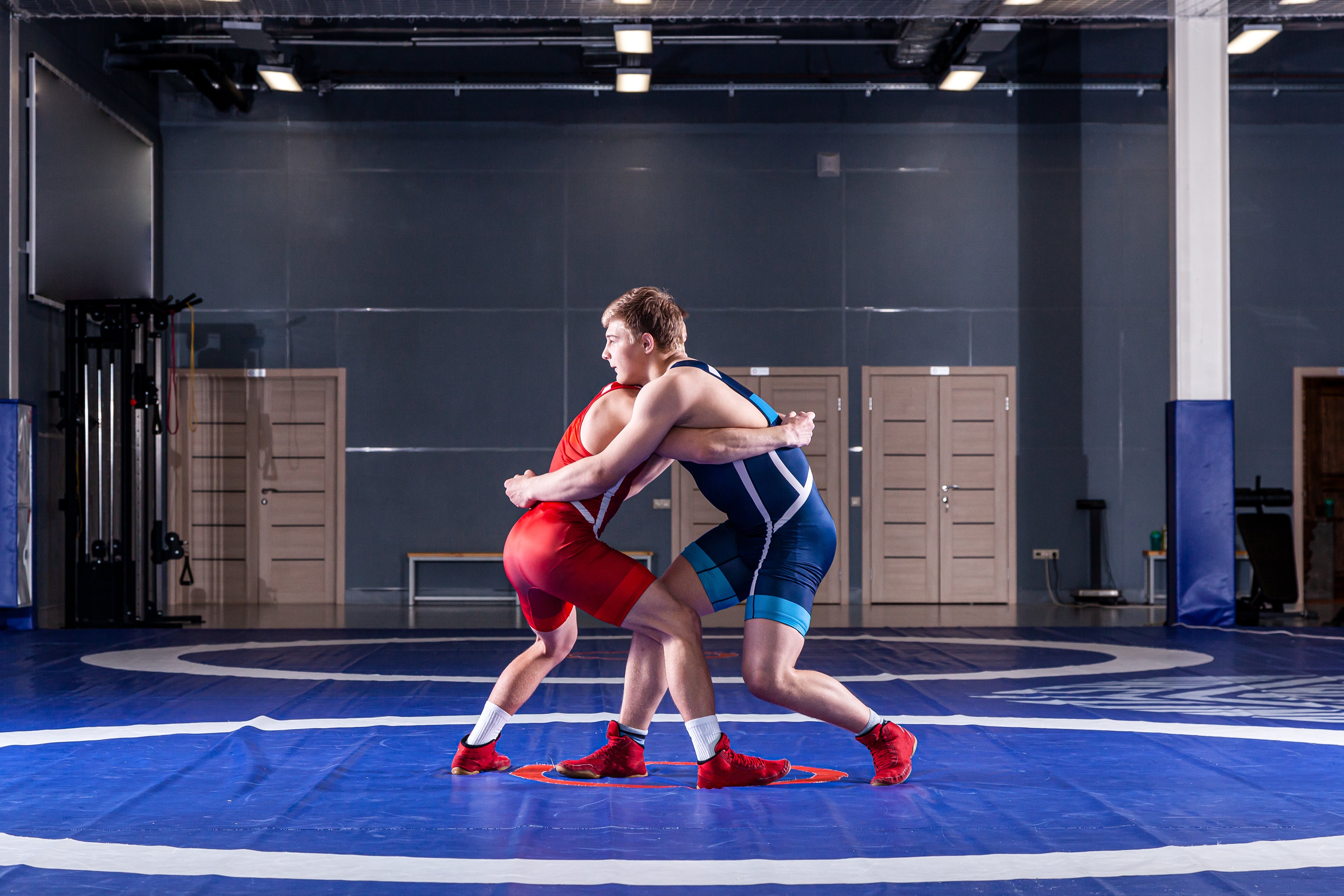 Two strong wrestlers in blue and red wrestling tights are wrestlng and making a  making a hip throw  on a yellow wrestling carpet in the gym. Young man doing grapple.